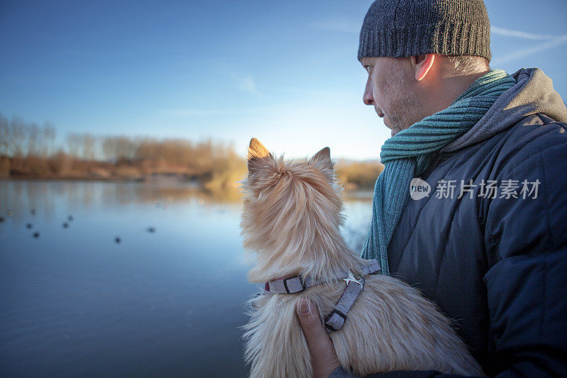 一个男人带着一只凯恩梗在湖边