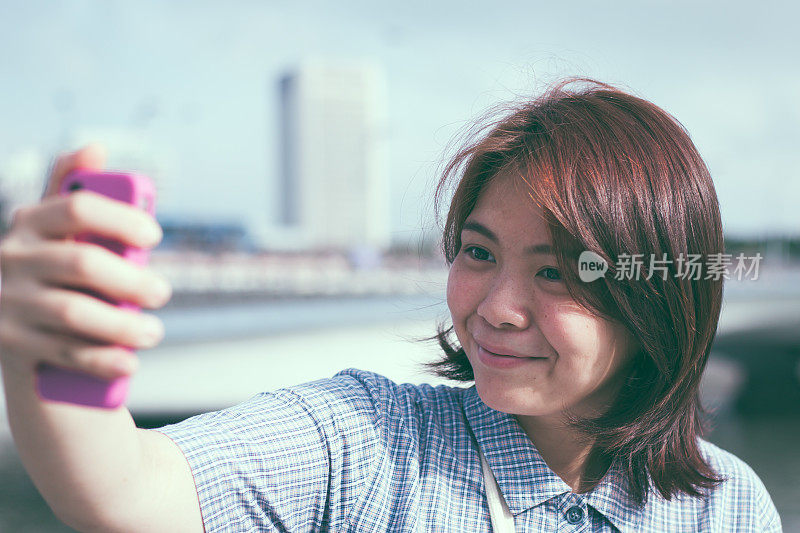 快乐的亚洲女孩用智能手机自拍。