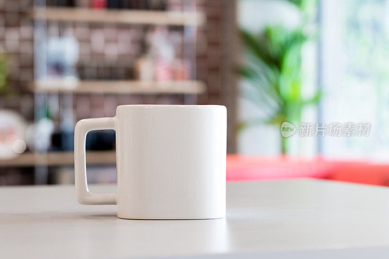 白色马克杯在早上的时间，在办公室的背景。为您设计的空白饮料杯。广场的形状。