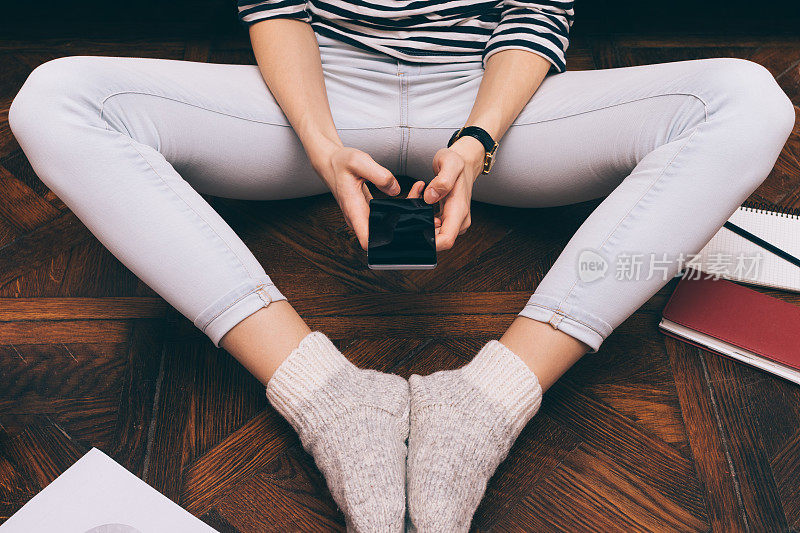 一个穿着牛仔裤的女孩坐在家里的地板上，用着智能手机