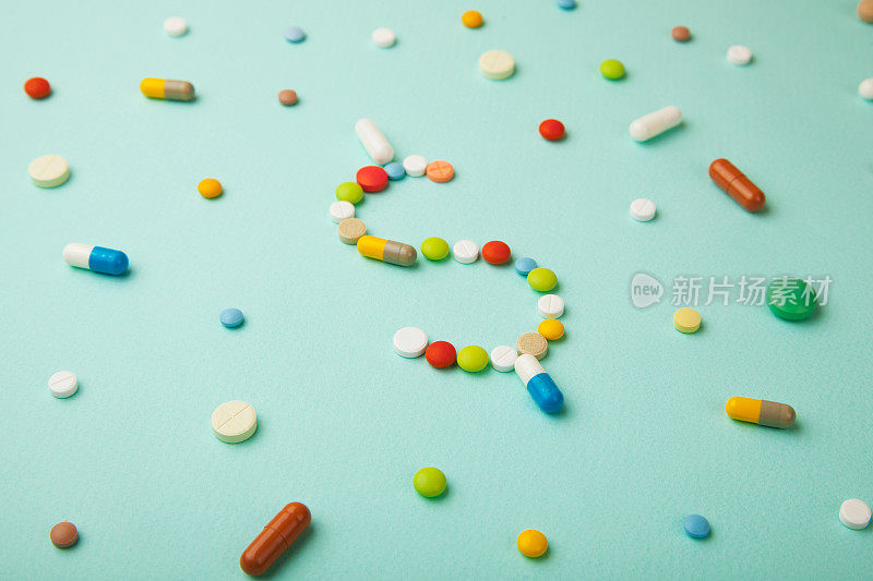 绿色背景上的彩色药丸和胶囊象征着金钱。昂贵的药品和医疗保险