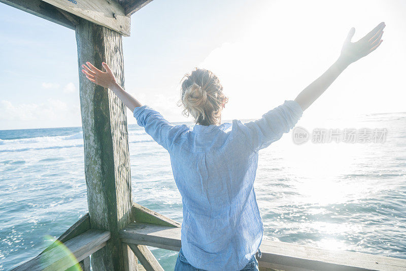 年轻女子在海上的木码头上享受海风