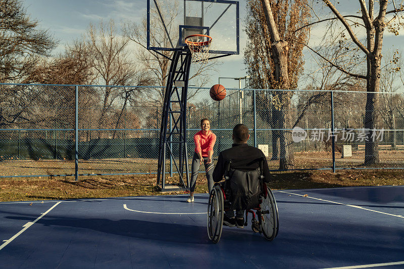 年轻的残疾人坐在轮椅上和他的妹妹打篮球