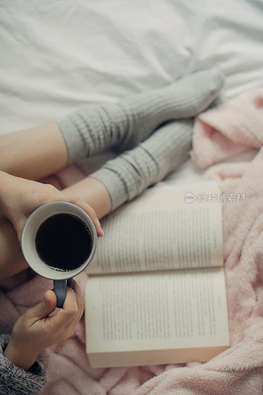 女人躺在床上，用一杯咖啡看书