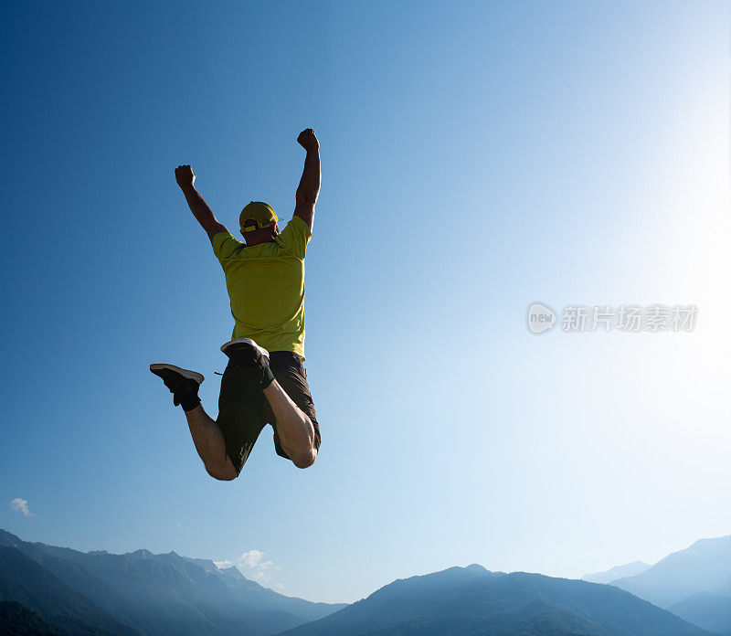 人举起手臂在空中跳。背景是山脊。