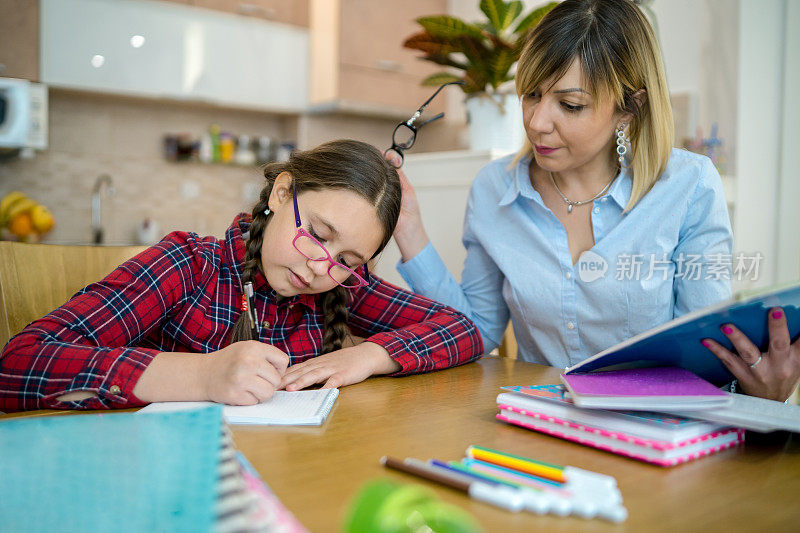 迷人的年轻女子和她可爱的小女儿正坐在桌旁一起做作业。母亲帮助女儿学习学校课程。