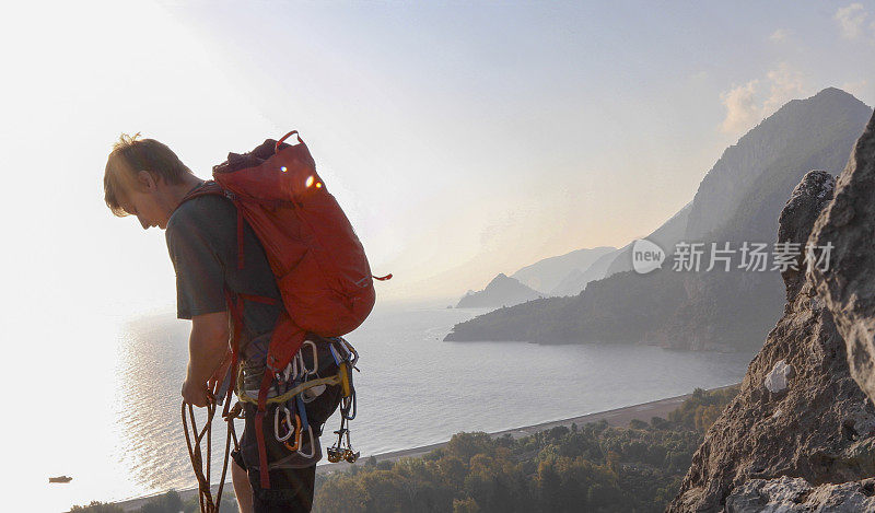 男性登山运动员在日出时爬上岩石顶峰