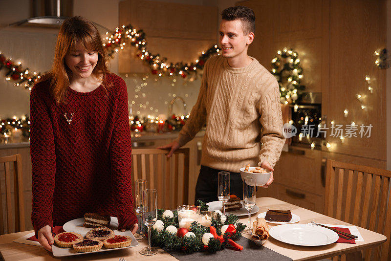 一对年轻夫妇在厨房布置圣诞餐桌。