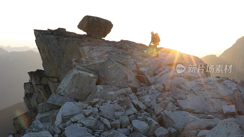 登山者在日出时徒步爬上岩石的顶峰