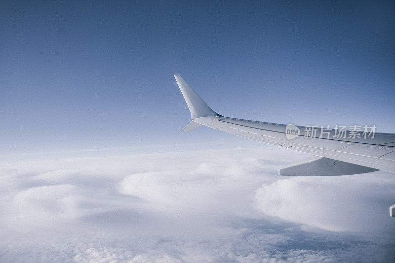 飞机的机翼，透过窗户看到多云的天空