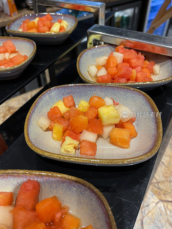 酒店自助早餐图片，展示了成熟的菠萝丁，蜜瓜和木瓜(木瓜)水果沙拉，高视图，重点在前景