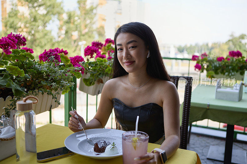友好的越南年轻女子在咖啡馆里摆姿势，一边吃着巧克力软糖蛋糕和冰淇淋。开朗的东南亚女性在露台上享用午餐时的甜点