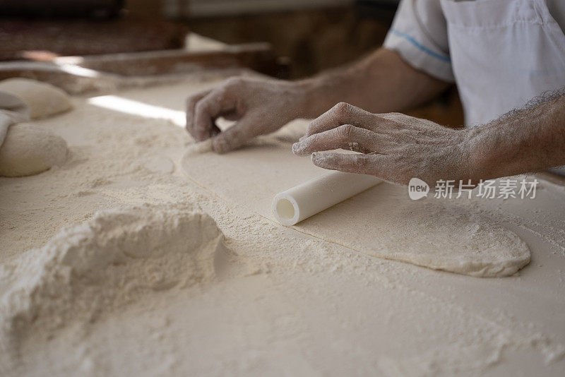 一个老人在面包店做面包，把面团铺好