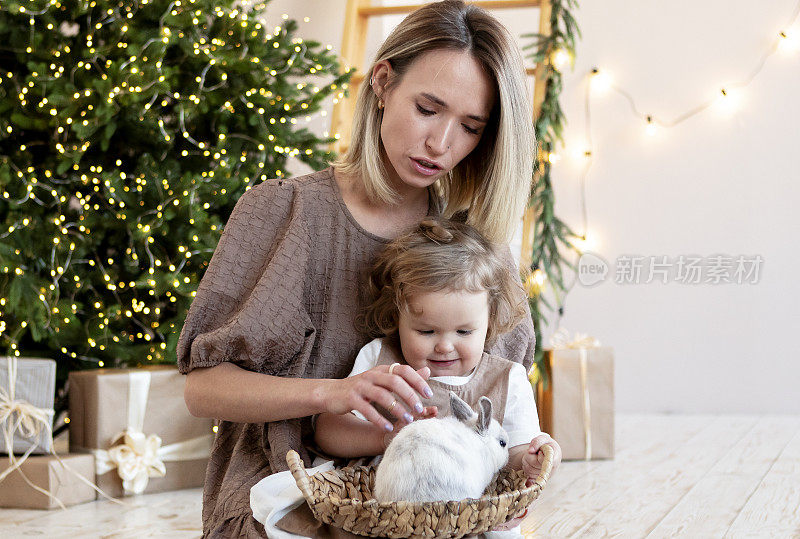 年轻的母亲和她金发碧眼的女儿在家里的圣诞树旁用礼物庆祝圣诞节。