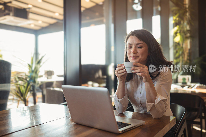 一位美丽的女商人坐在咖啡馆里，用笔记本电脑享受着她最喜欢的咖啡