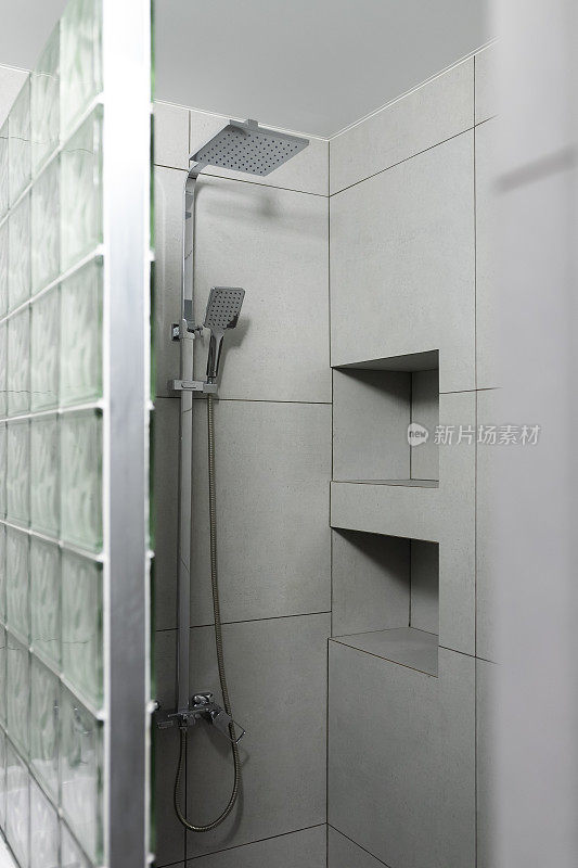 现代浴室内部与极简主义的照明。淋浴区。雨淋间，石膏板架子上排列着瓷石器
