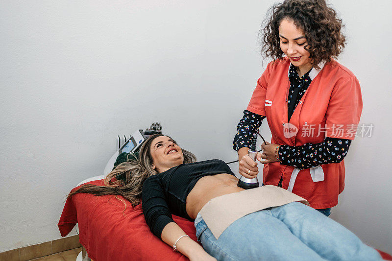 一个女人躺在治疗台上，美容师正在给她做减肥手术。