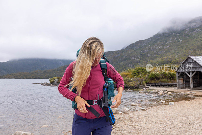 绿洲山:一个女徒步旅行者调整她的背包，暂停在雄伟的山峰湖