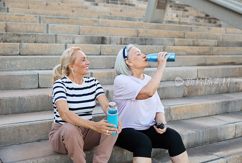 积极的老年人朋友在运动场上锻炼后在楼梯上放松，喝着瓶装水