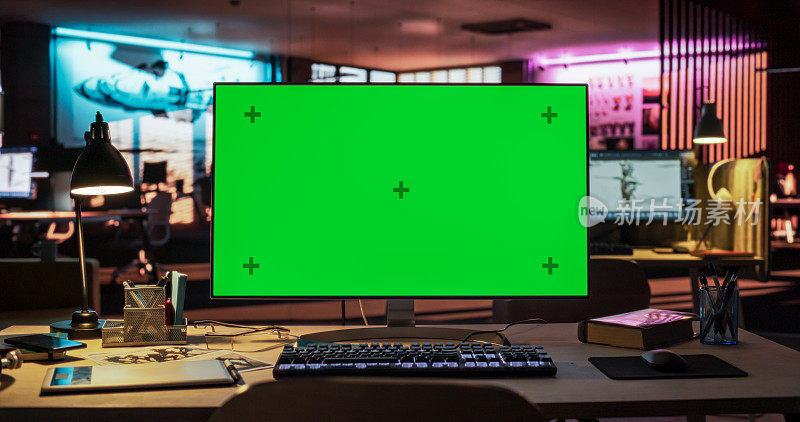 站在霓虹灯照亮的空荡荡的创意办公室的桌子上，模拟绿屏色度键显示的台式电脑。游戏开发或动画公司主管