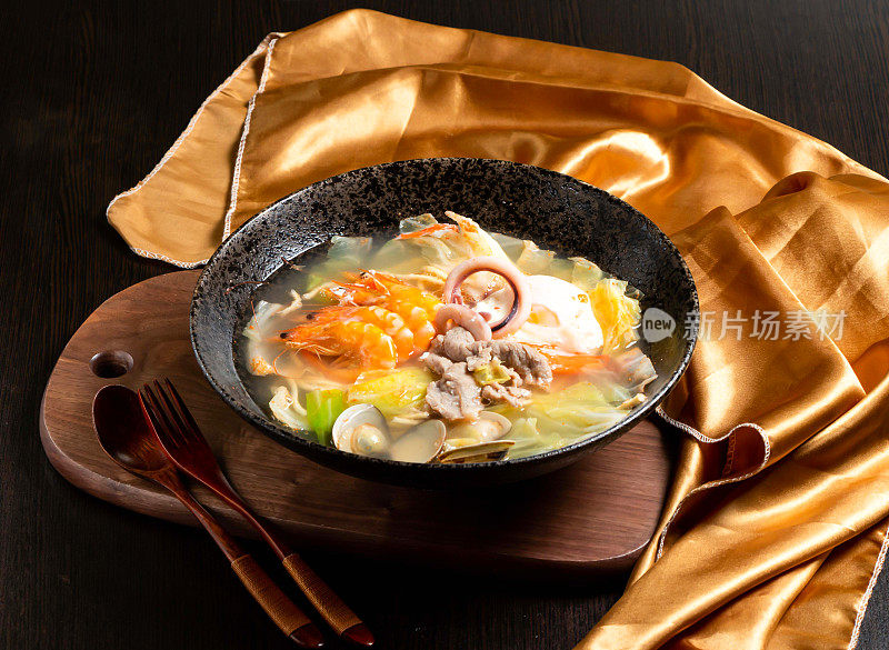 海鲜和鸡肉炖虾，鱿鱼圈，叉子和勺子在盘子里孤立的木板亚洲食品的侧视图
