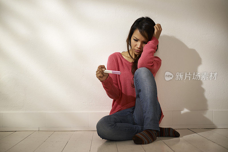悲伤的亚洲女孩坐在地板上看验孕棒