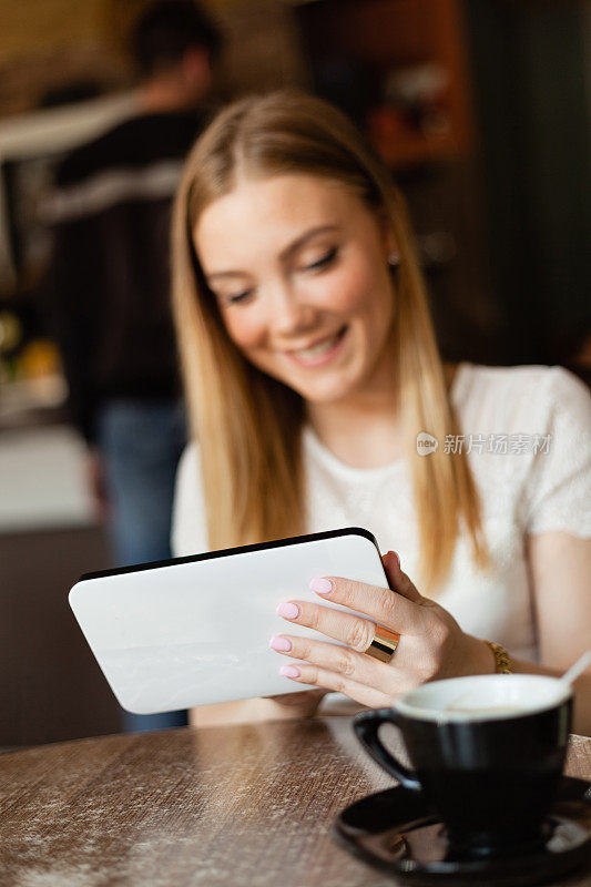 美丽的年轻女孩使用数字平板电脑在咖啡馆