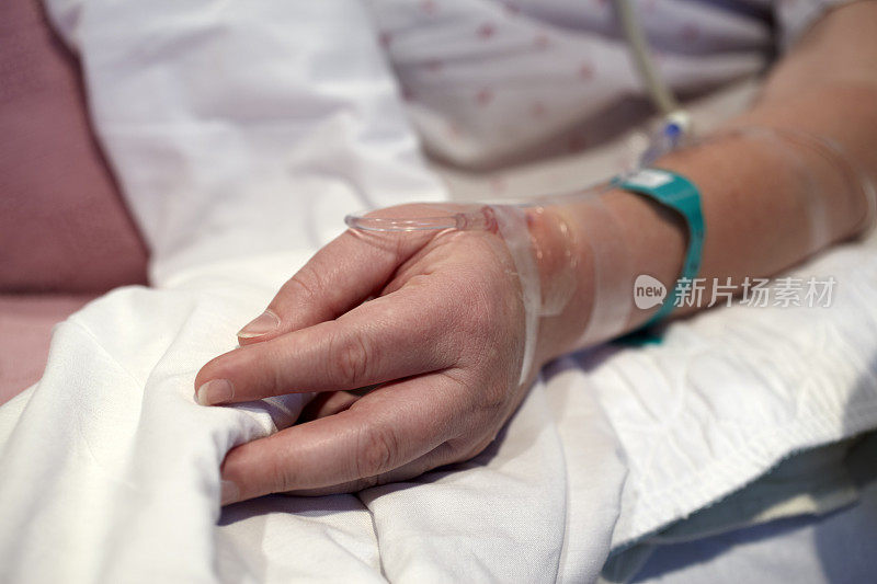 病床上女性患者的手与静脉滴注管