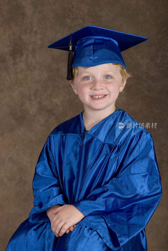 幼儿园毕业照，可爱的小男孩拿着学士服和学士帽