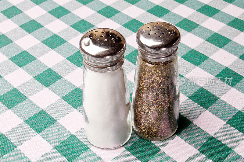 盐和胡椒瓶在绿色格子布上