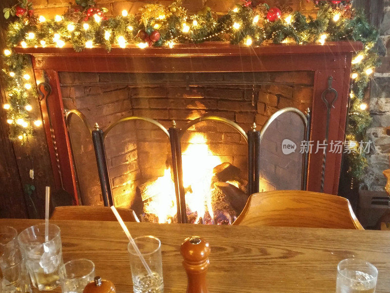 木制餐桌，舒适的冬季火，砖壁炉，圣诞花环