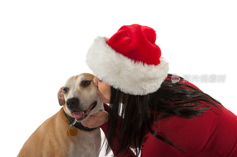 戴着圣诞帽亲吻狗的年轻女人