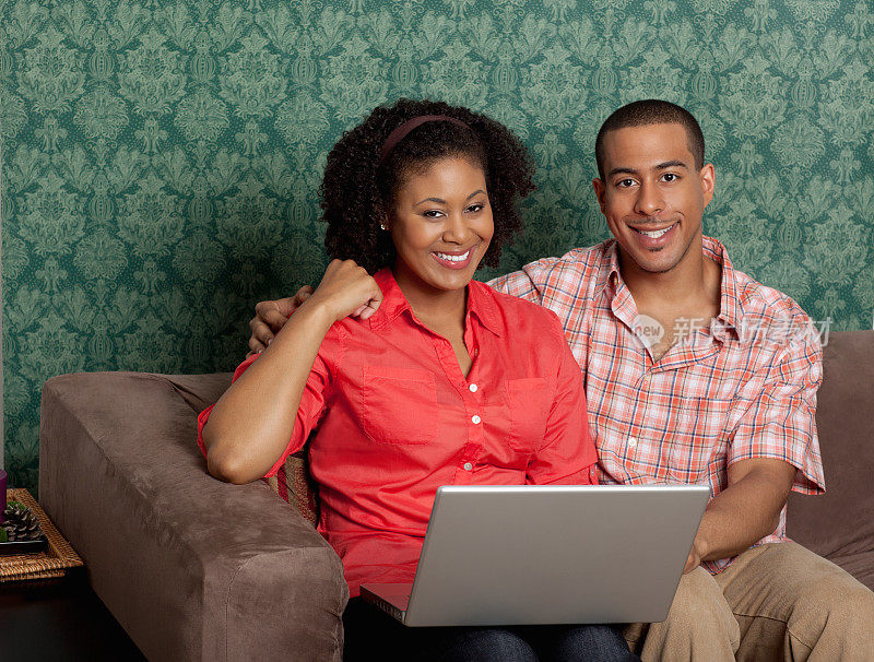 一对年轻夫妇拿着笔记本电脑坐在家里的沙发上