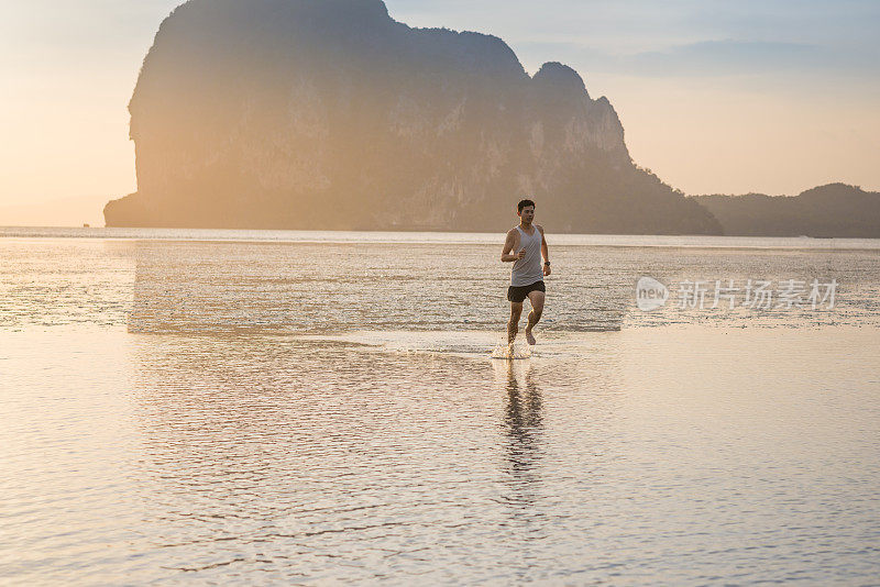 年轻的亚洲男子在海滩上奔跑，夕阳为背景