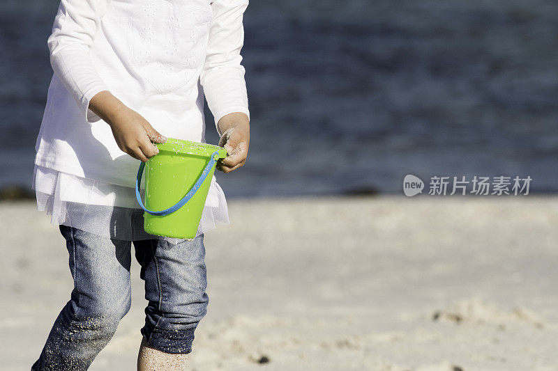 中景小女孩提着一桶海水上了海滩。