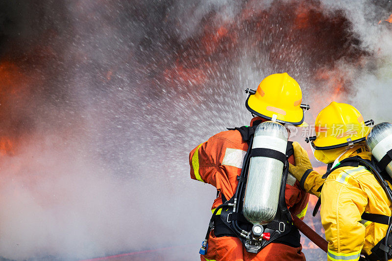 两名消防队员用高压水枪将水喷向火焰周围有烟雾和拷贝空间