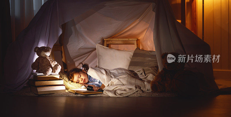 小女孩睡在帐篷里，带着书和手电筒