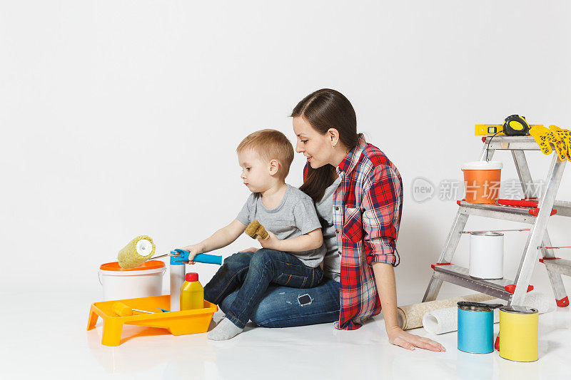 母亲和年幼的儿子用仪器装修公寓房间隔离在白色的背景上。墙纸，胶水配件，绘画工具。修理家的男孩女人。父母的童年概念。