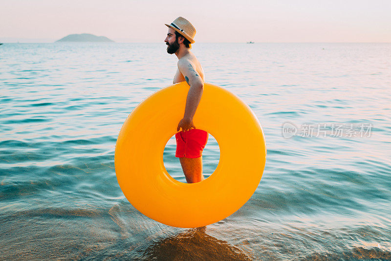 一个戴着帽子的英俊的胡子男人在海边享受着阳光明媚的夏日