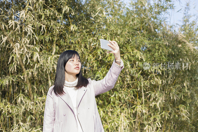 一名女子靠着一堵大篱笆用智能手机拍照
