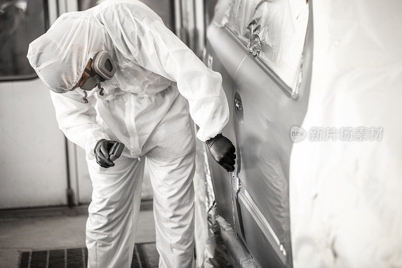修理技术员在白色工装裤检查油漆的一致性在一个修理室的汽车部分