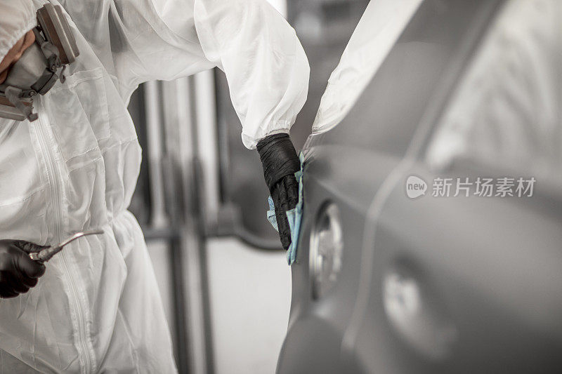 汽车修理技术员在汽车喷漆室中，在汽车的四分之一的面板上涂上一层透明的涂层