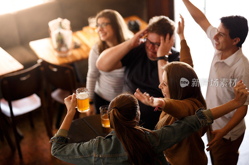 朋友们在电视上看体育节目，在酒吧里喝啤酒