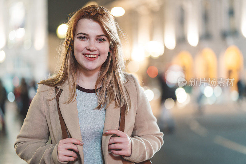 晚上在皮卡迪利广场，年轻女子对着镜头微笑