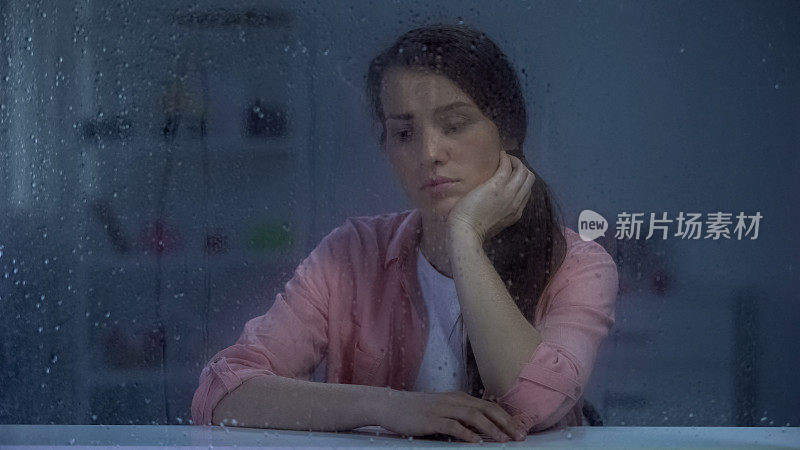 沉思的女人思考人生的问题，坐在雨窗后，烦恼