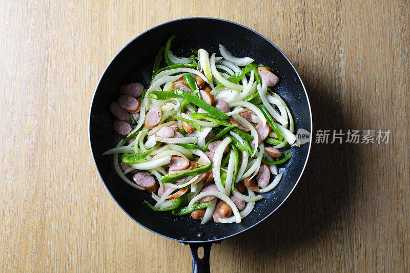 日式意面菜肴，意大利面(那不勒斯)的食谱和配料。浅棕色的木纹桌上有一个煎锅，里面放着辣椒、香肠、洋葱。