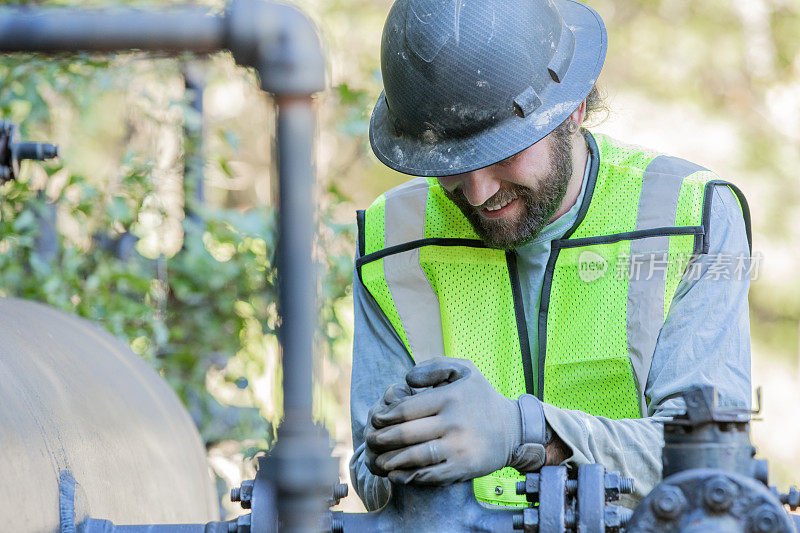 石油行业员工戴安全帽在石油管道附近的重型设备上工作