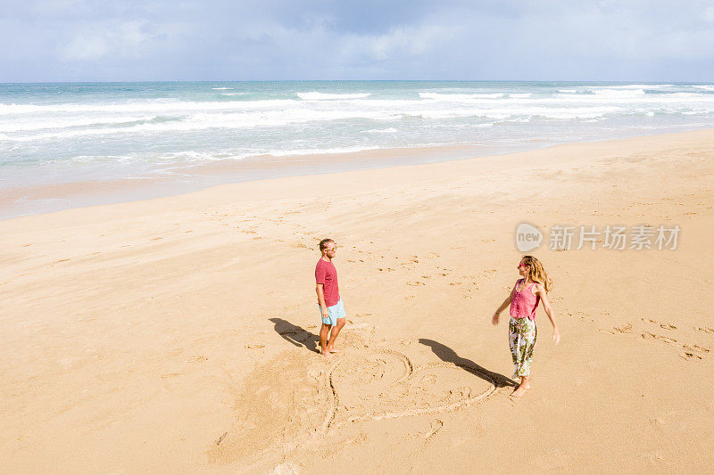 无人机上的年轻夫妇站在海滩上靠近画的心在沙滩上