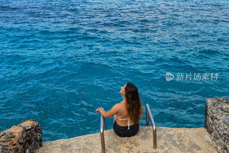 年轻女子坐在前面的水大海-凝视着大海