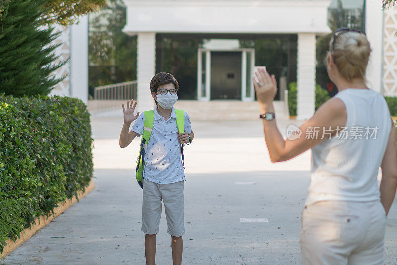 妈妈在学校前面挥手示意她的儿子。